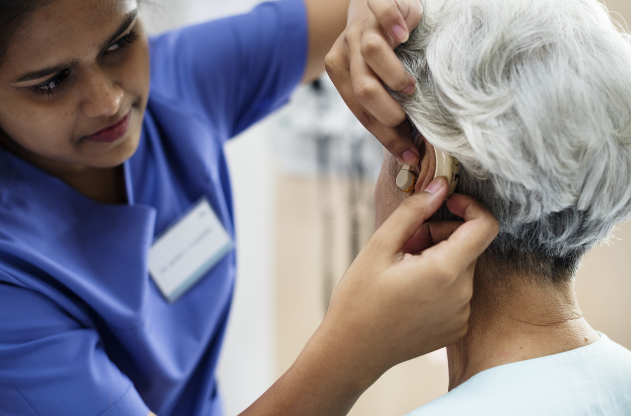 A female audiologist helping an elderly female patient with hearing aids repair.